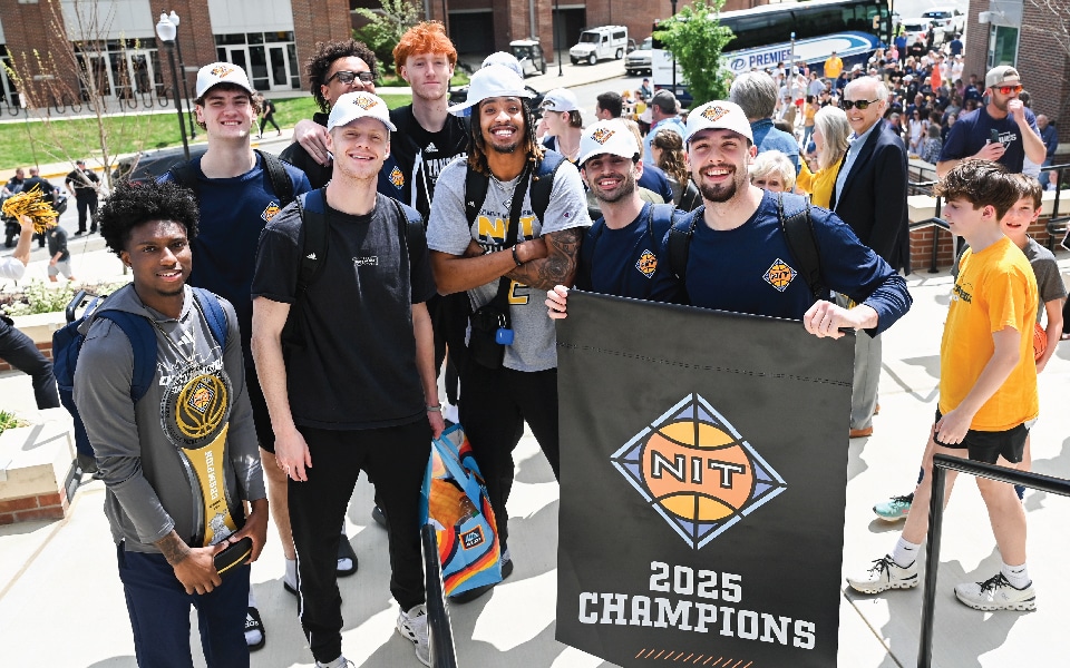 NIT Champions_960x600 Members of the Men's Basketball team pose with the NIT Championship banner and trophy ourside of McKenzie Arena