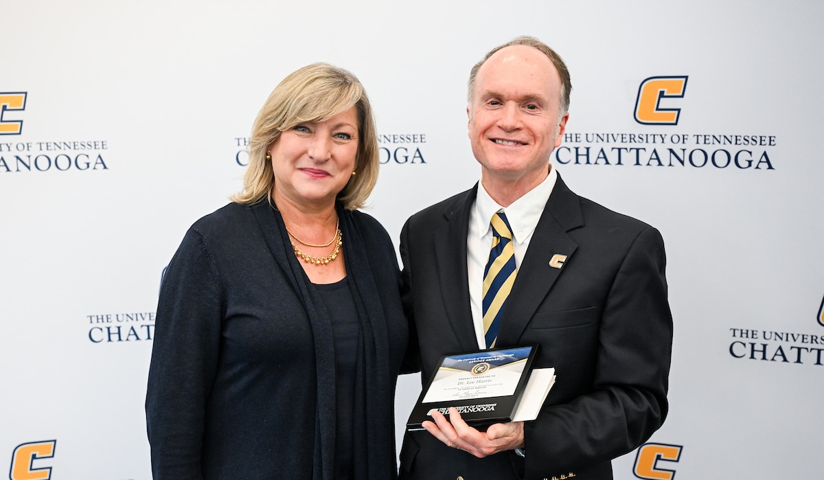 two people smiling at camera with one holding an award